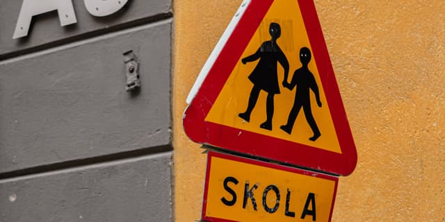 En skylt med två barn som det står skola på.