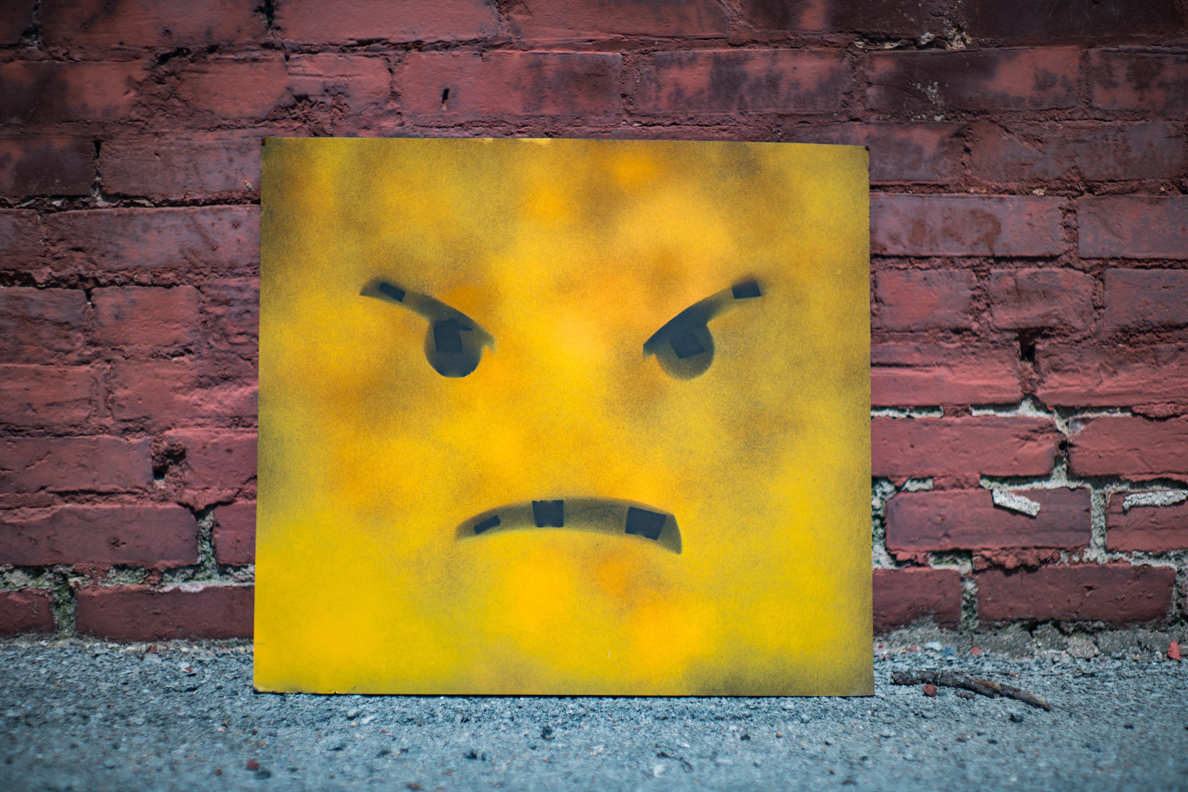 Bild på en sur emoji som står lutad mot en tegelvägg.